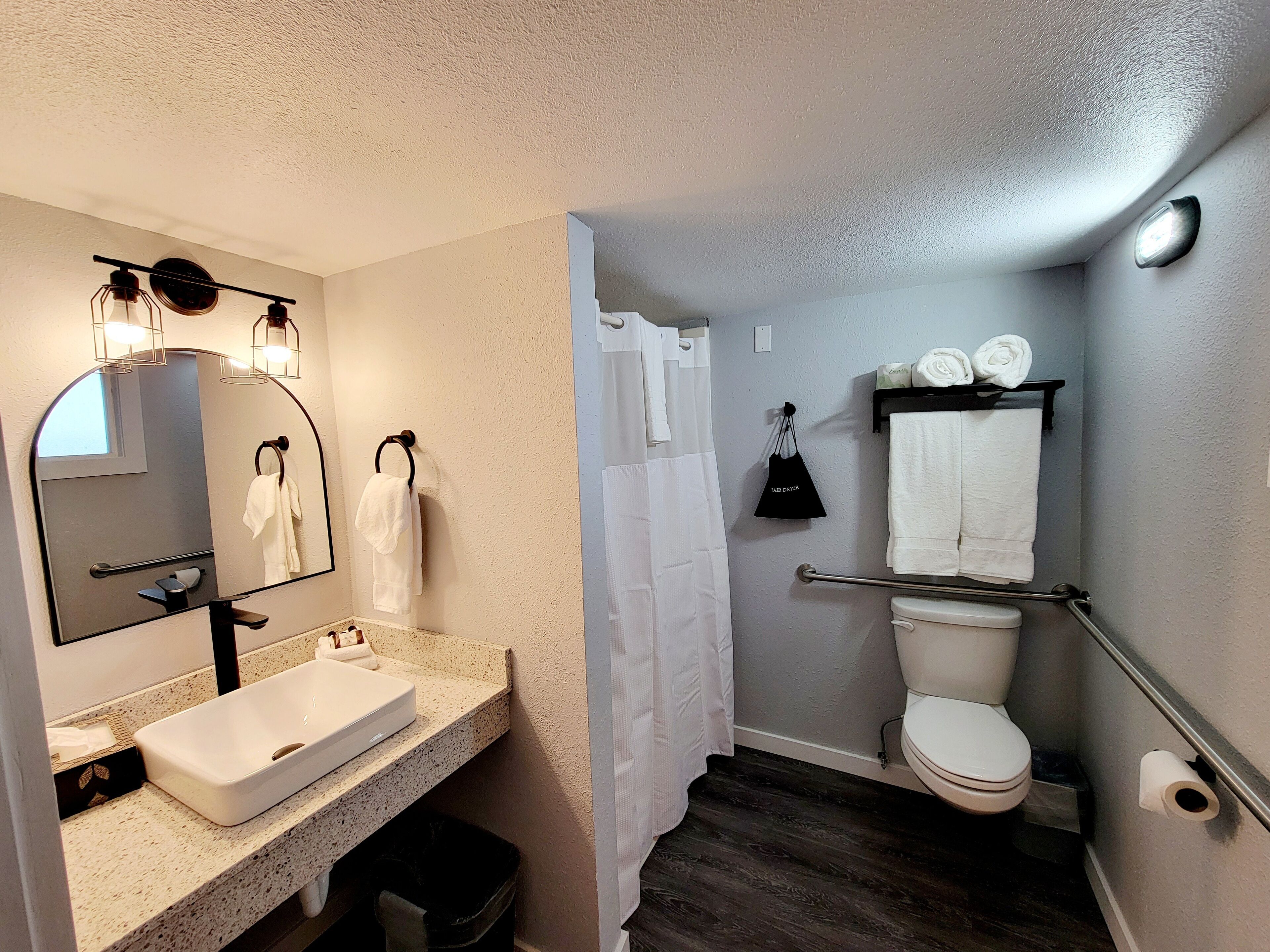 A bathroom with a white sink, a mirror, a towel rack, a toilet, and a shower curtain.