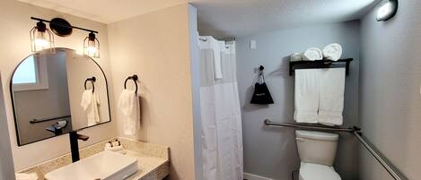 A bathroom with a white sink, a mirror, a towel rack, a toilet, and a shower curtain.