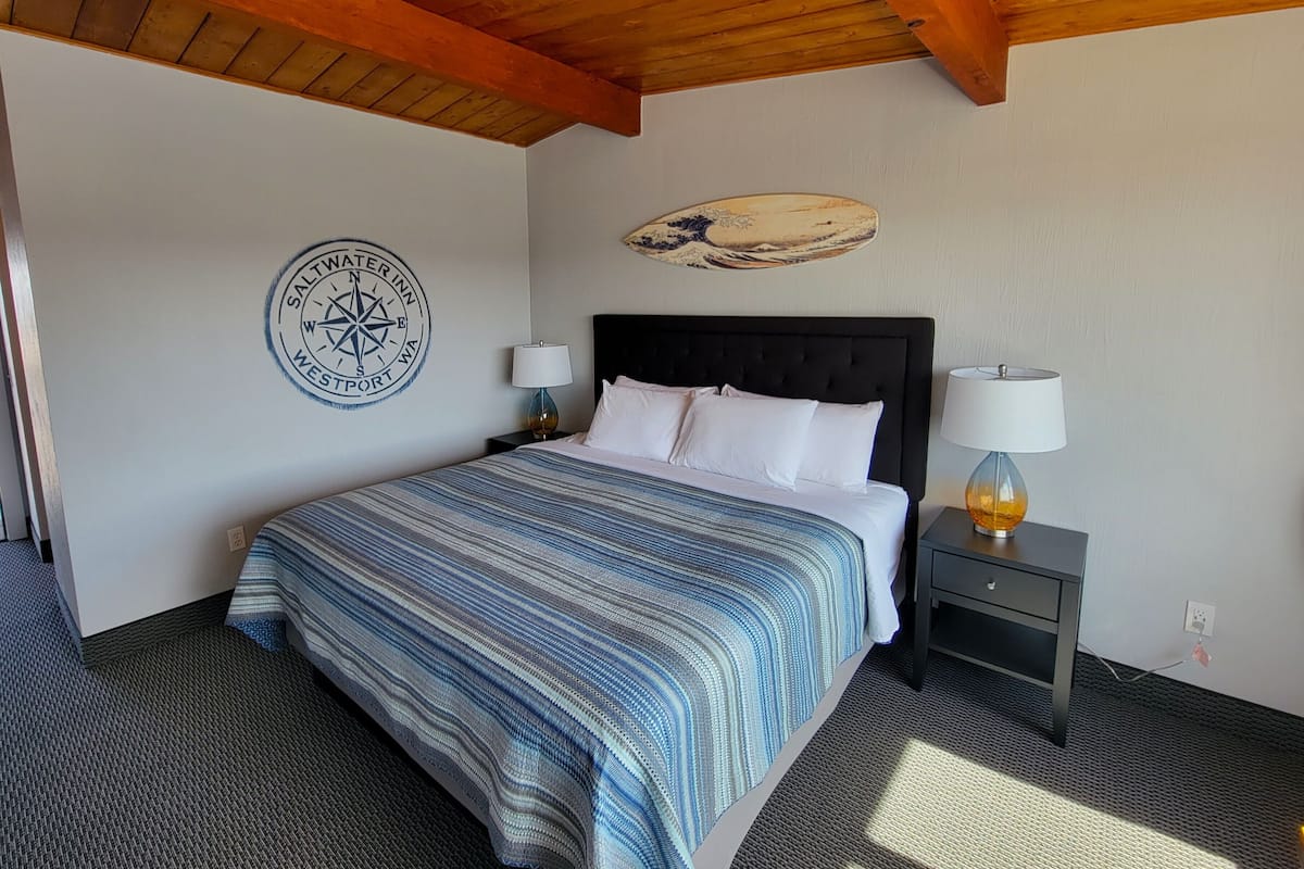 A hotel room with a large bed, a compass wall decoration, a wooden ceiling, and a nightstand with a lamp.
