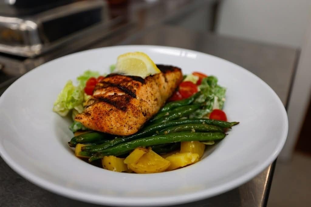 A plate of grilled salmon with asparagus and pineapple, garnished with a lemon wedge.