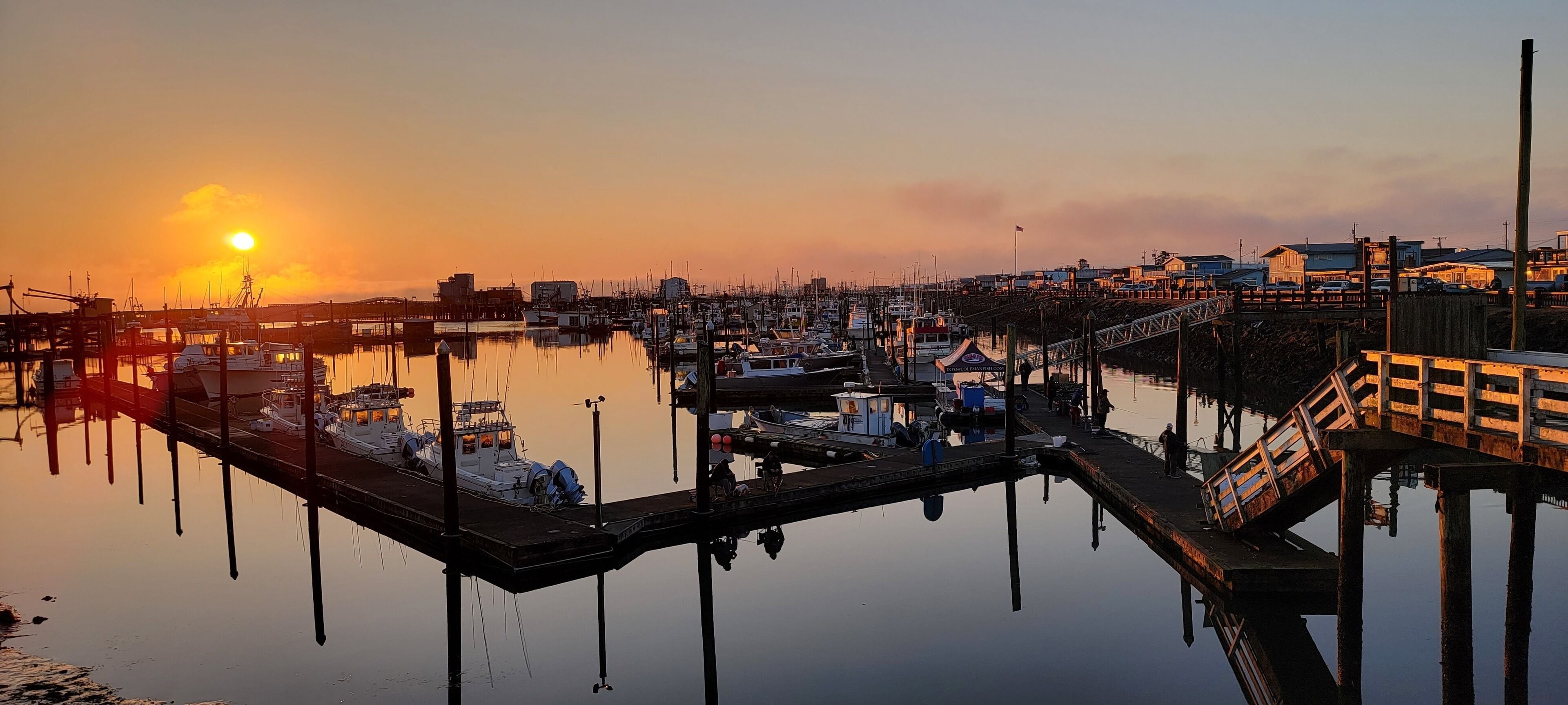 A marina with boats docked, a pier, and buildings in the background.