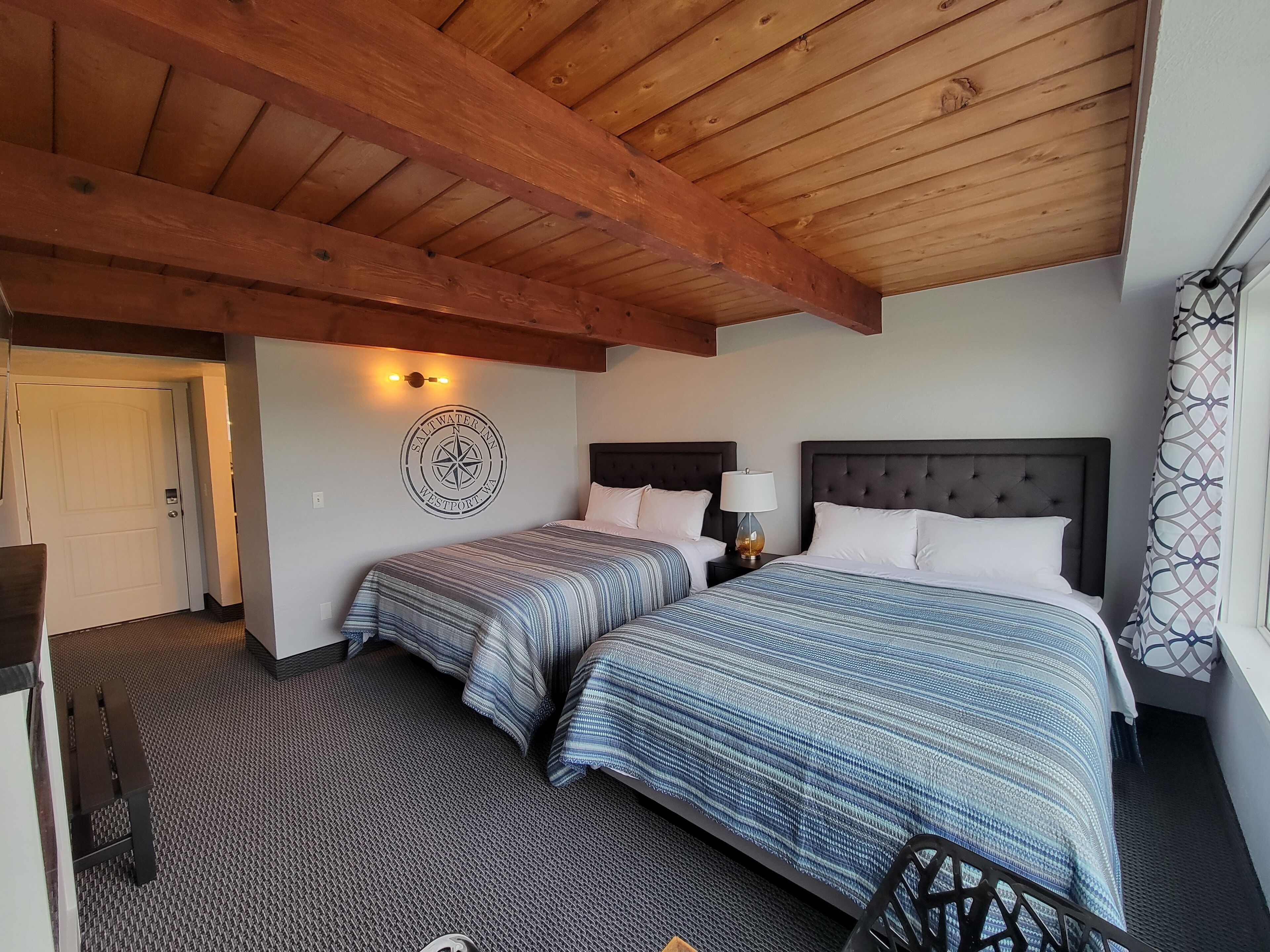 Une chambre d’hôtel avec deux lits, un plafond en bois, une décoration murale représentant une boussole et une moquette à motifs.