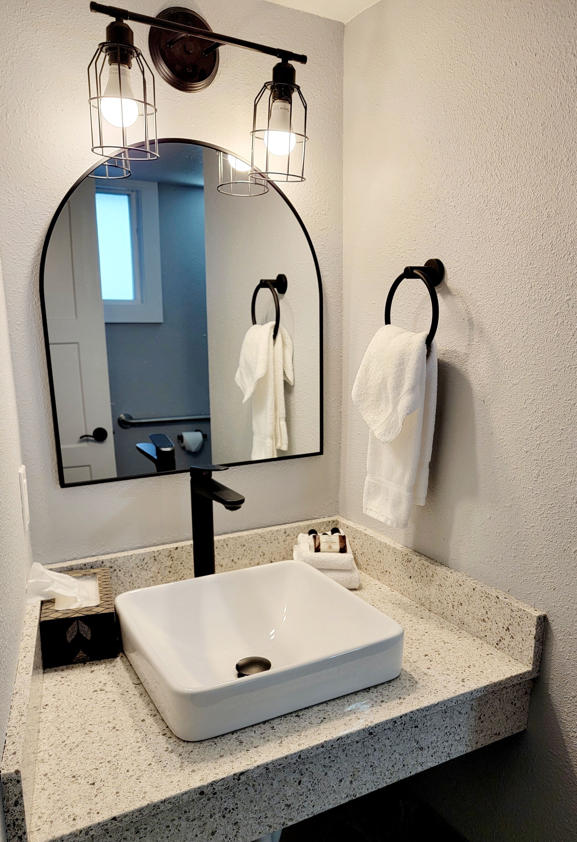 A bathroom with a white sink, a large mirror, and two towel rings.