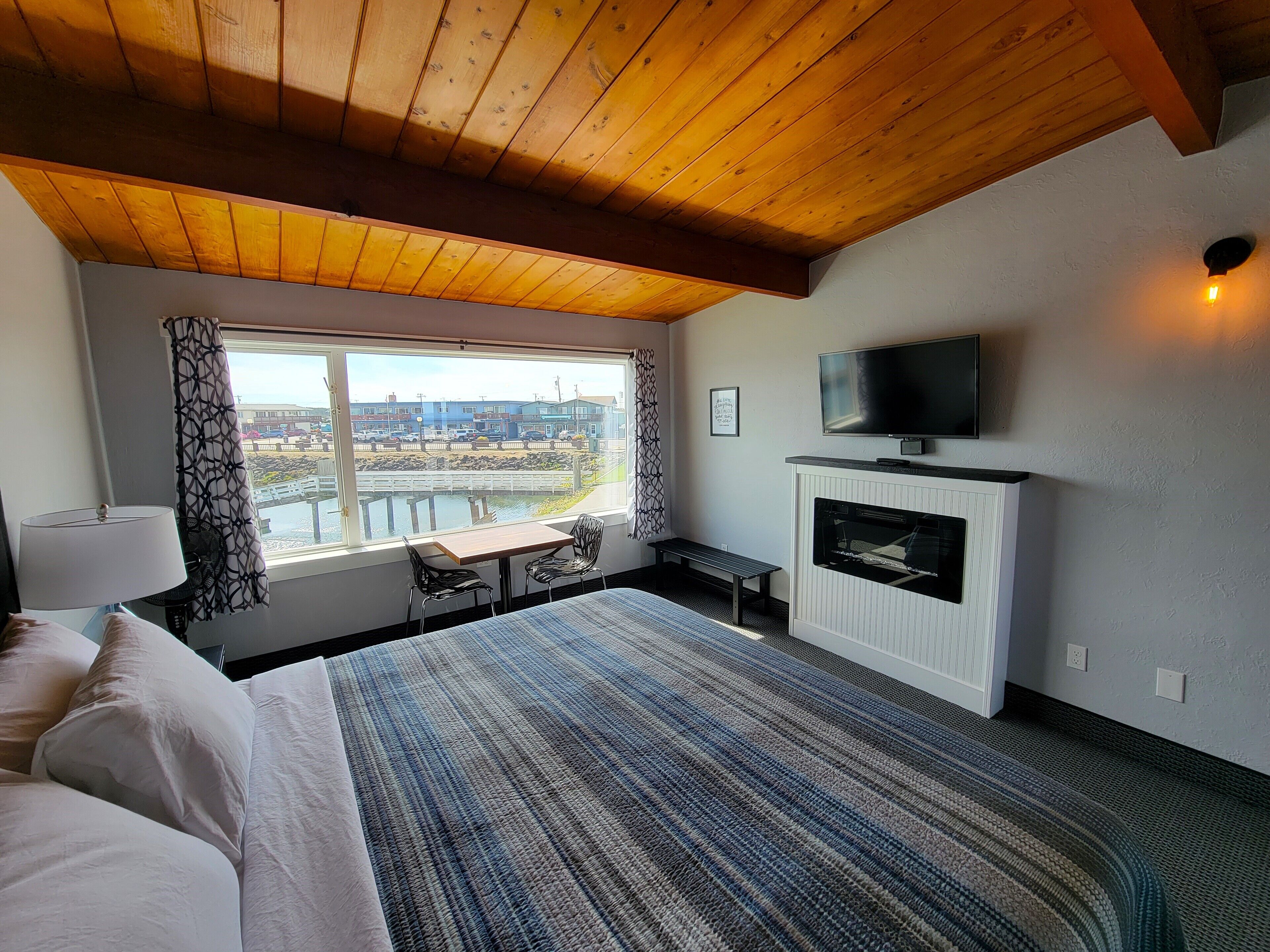 A bedroom with a large bed, a TV, a fireplace, a window with a view, and a patterned carpet.