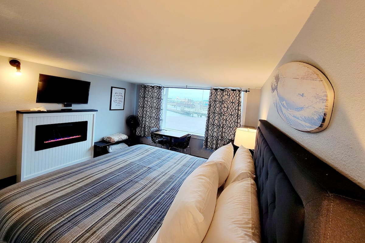 A hotel room with a bed, a flat-screen TV, a desk, and a window with curtains.