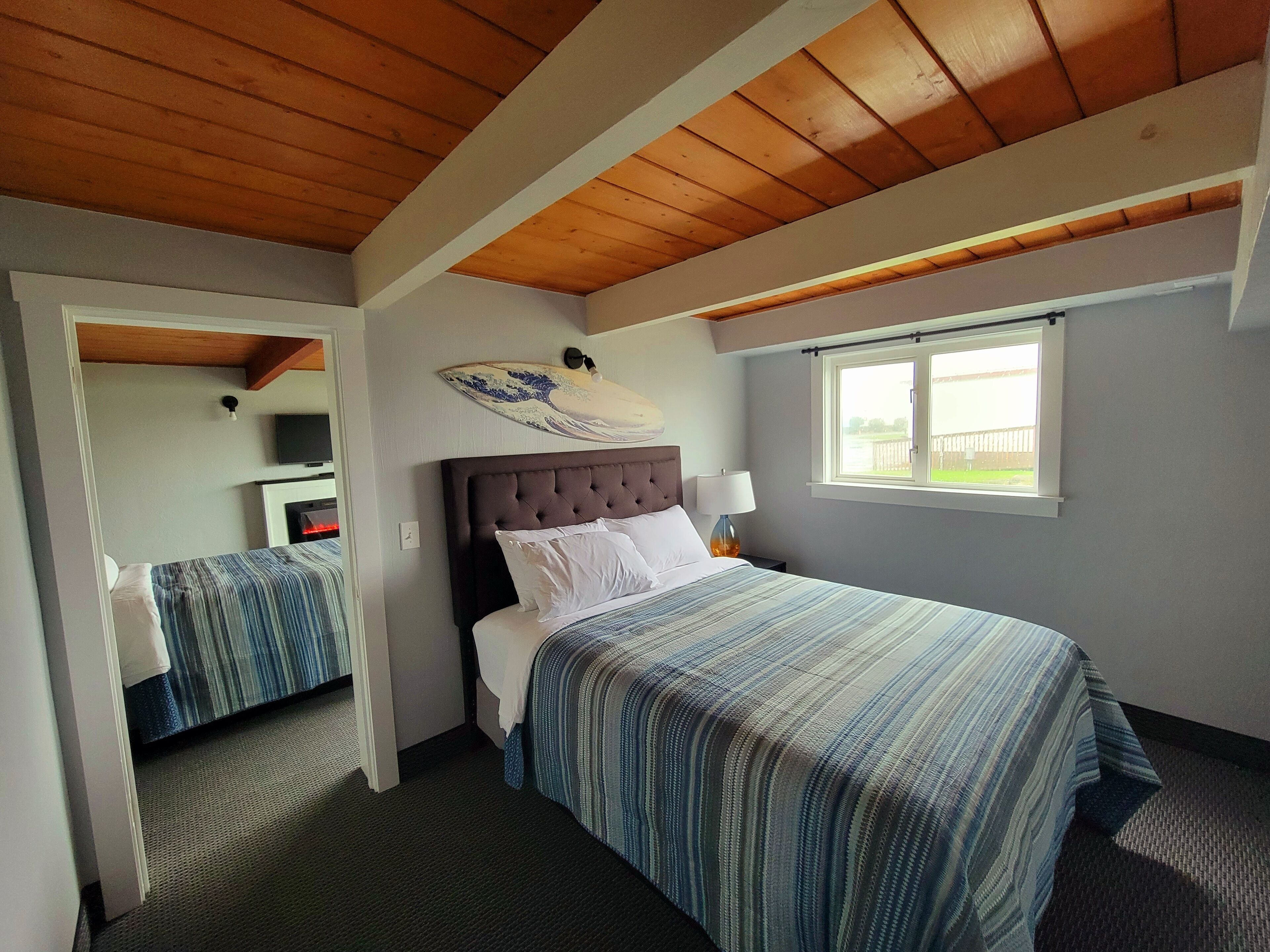 A bedroom with a large bed, a smaller bed, a window, and a wooden ceiling.