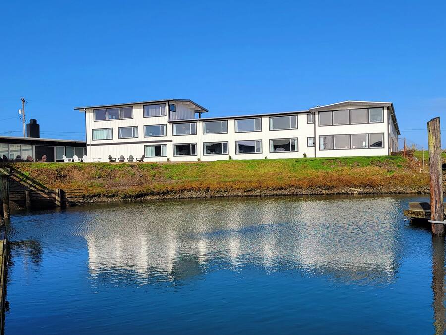 A modern multi-story building with large windows and a flat roof, situated next to a calm body of water.