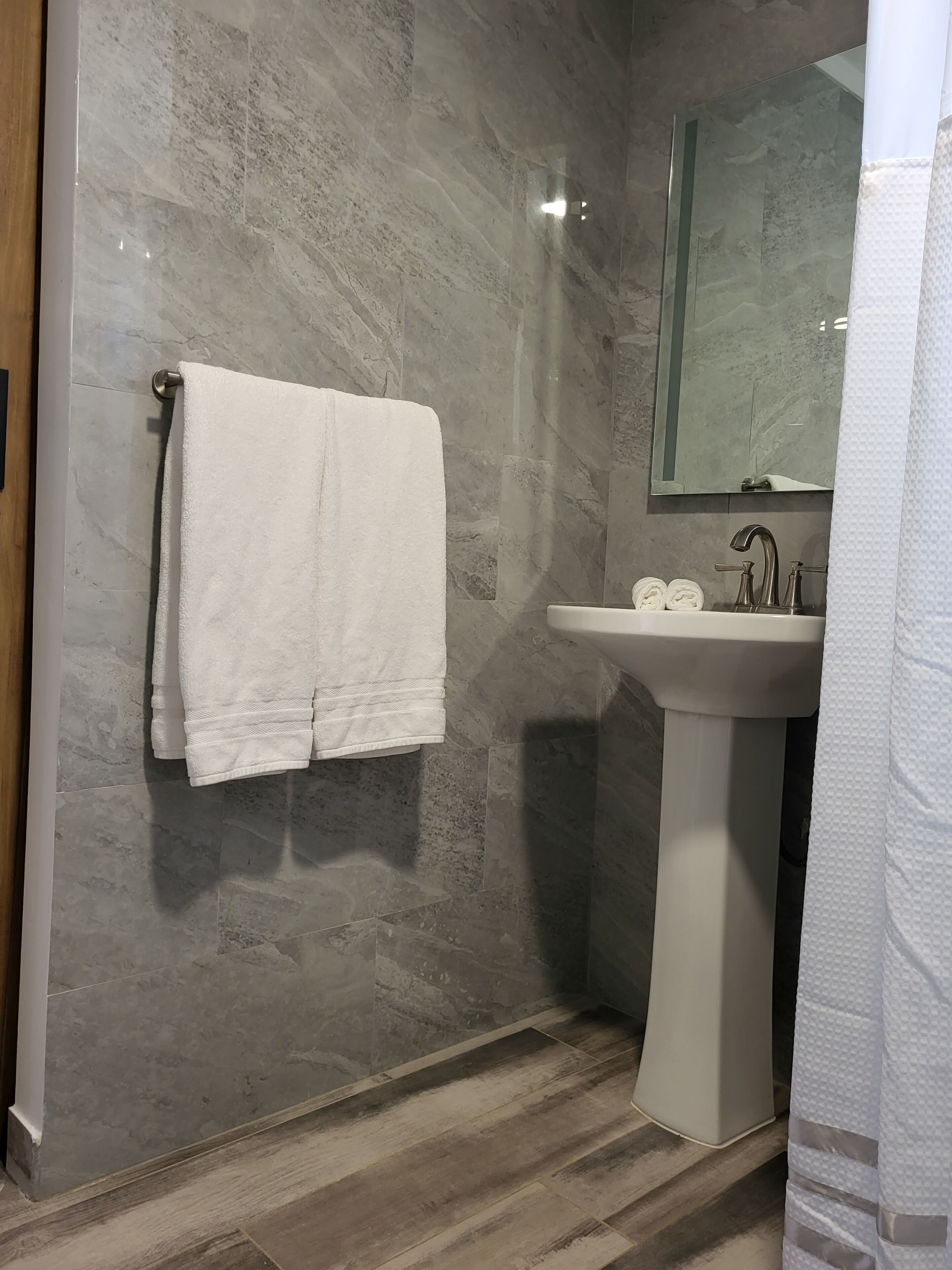 A bathroom with a marble wall, a white sink, and a towel hanging on the wall.