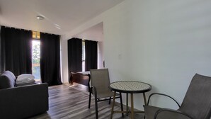 A modern living room with a sofa, a round table, and a chair. There is a window with curtains, a door, and a view of the outside. - Tierra Adentro Bed & Breakfast (Naguabo)