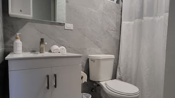 Un baño moderno con pared de mármol, un lavamanos blanco con dispensador de jabón, un inodoro y una cortina de ducha.