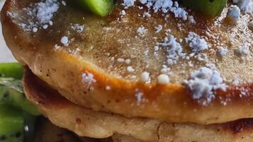 Una pila de tortitas con rodajas de kiwi y azúcar glas.