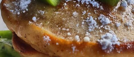 A stack of pancakes with kiwi slices and powdered sugar.