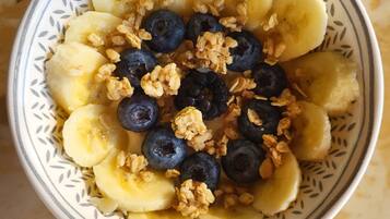 A bowl of fruit salad with bananas, blueberries, and granola on a patterned plate.