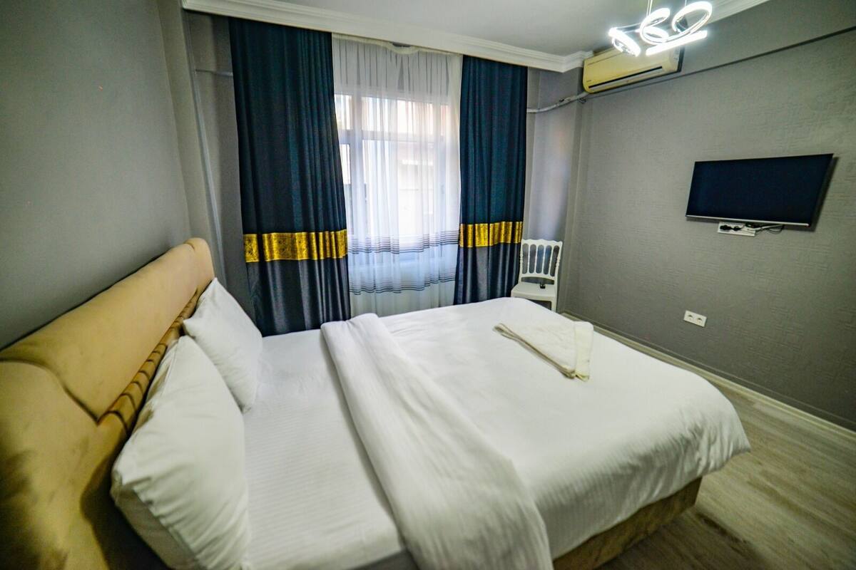 Una habitación de hotel con cama, cortinas, televisor y aire acondicionado.