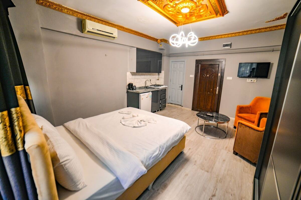 Habitación de hotel con cama, una kitchenette pequeña, una mesa de comedor, un televisor y una puerta.
