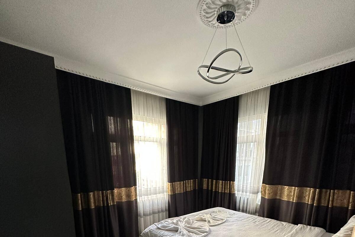 Un dormitorio con una cama grande, cortinas oscuras con detalles dorados, suelo de madera y un ventilador de techo.