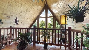 A wooden cabin with a balcony, potted plants, and a view of the outdoors.