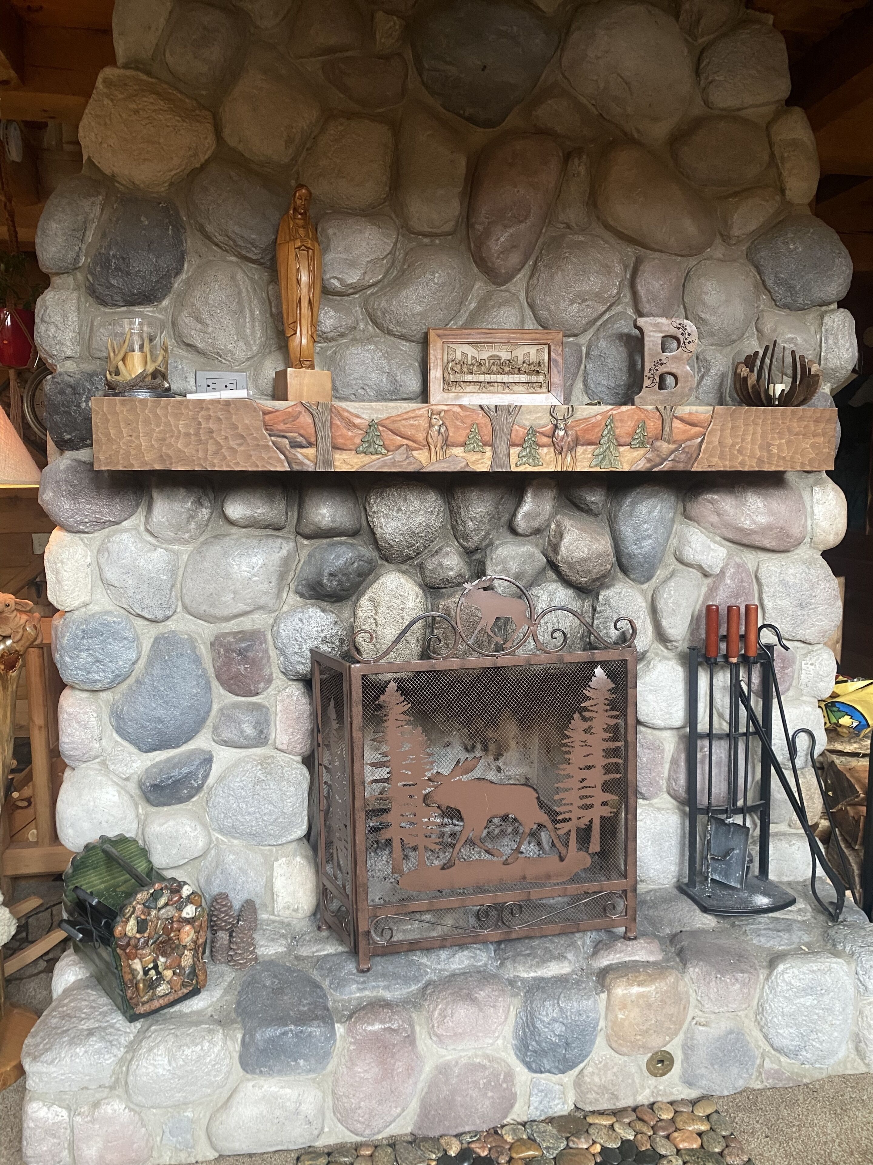 A stone fireplace with a wooden mantel, a framed artwork, and a decorative metal piece.