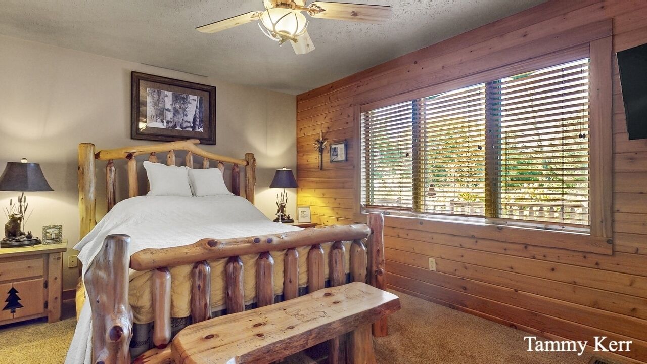 Ein Schlafzimmer mit einem Holzbettgestell, einer Bank, einem Deckenventilator und einem großen Fenster mit Jalousien.