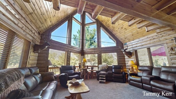 A log cabin interior with a high ceiling, large windows, and leather furniture.