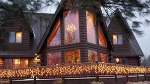 A log cabin with large windows and a porch decorated with string lights.