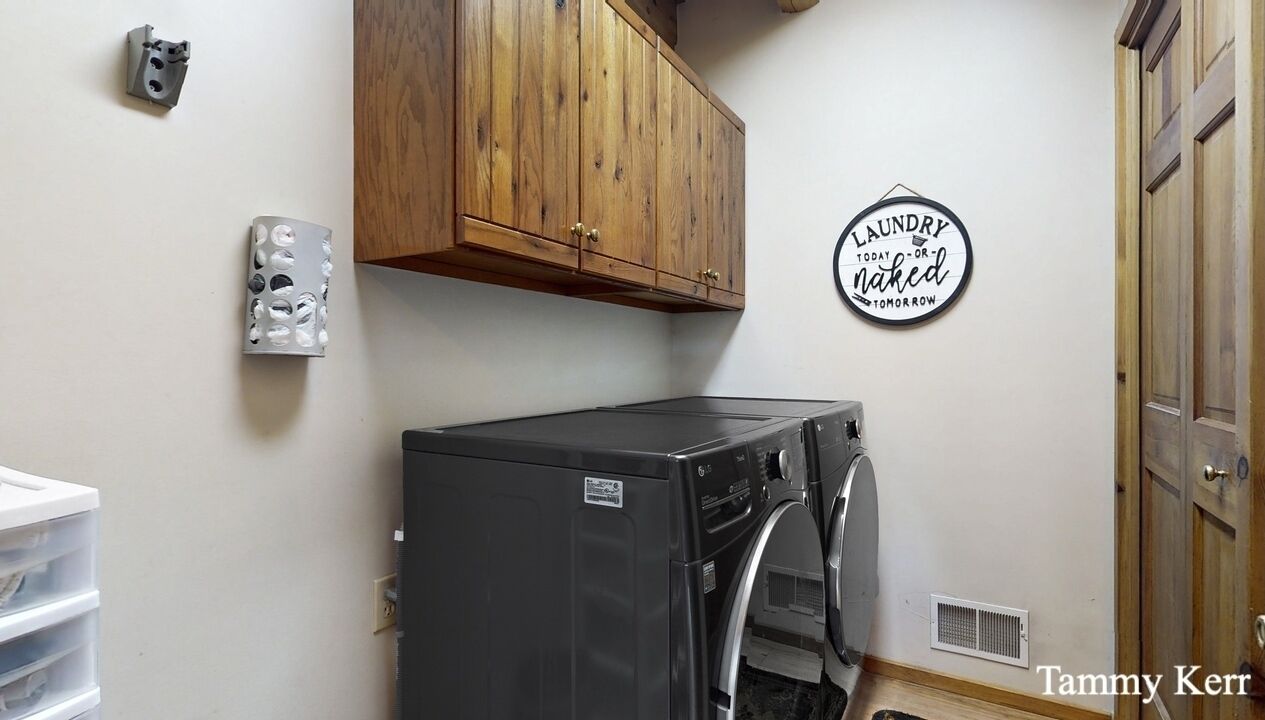 A laundry room with a washing machine, wooden cabinets, a wall-mounted laundry sign, and a vent.