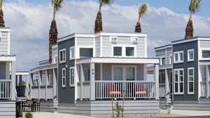 Une rangée de maisons de plage modernes à deux étages, dotées de balcons, bordée de palmiers, et avec un ciel dégagé.