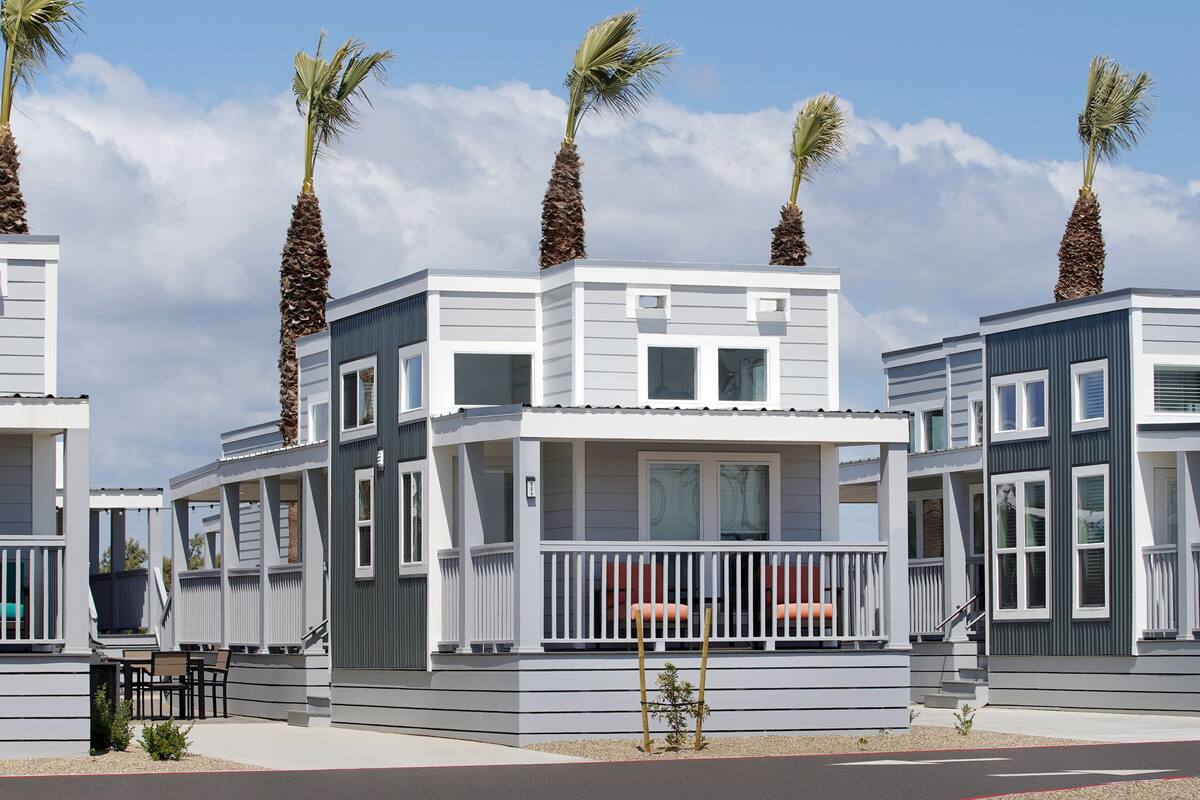 A row of modern, two-story beach houses with balconies, palm trees, and a clear sky.