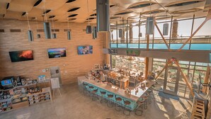 Un espace bar moderne doté d’un long comptoir, de nombreux tabourets et offrant une vue sur la ville grâce à de grandes fenêtres.