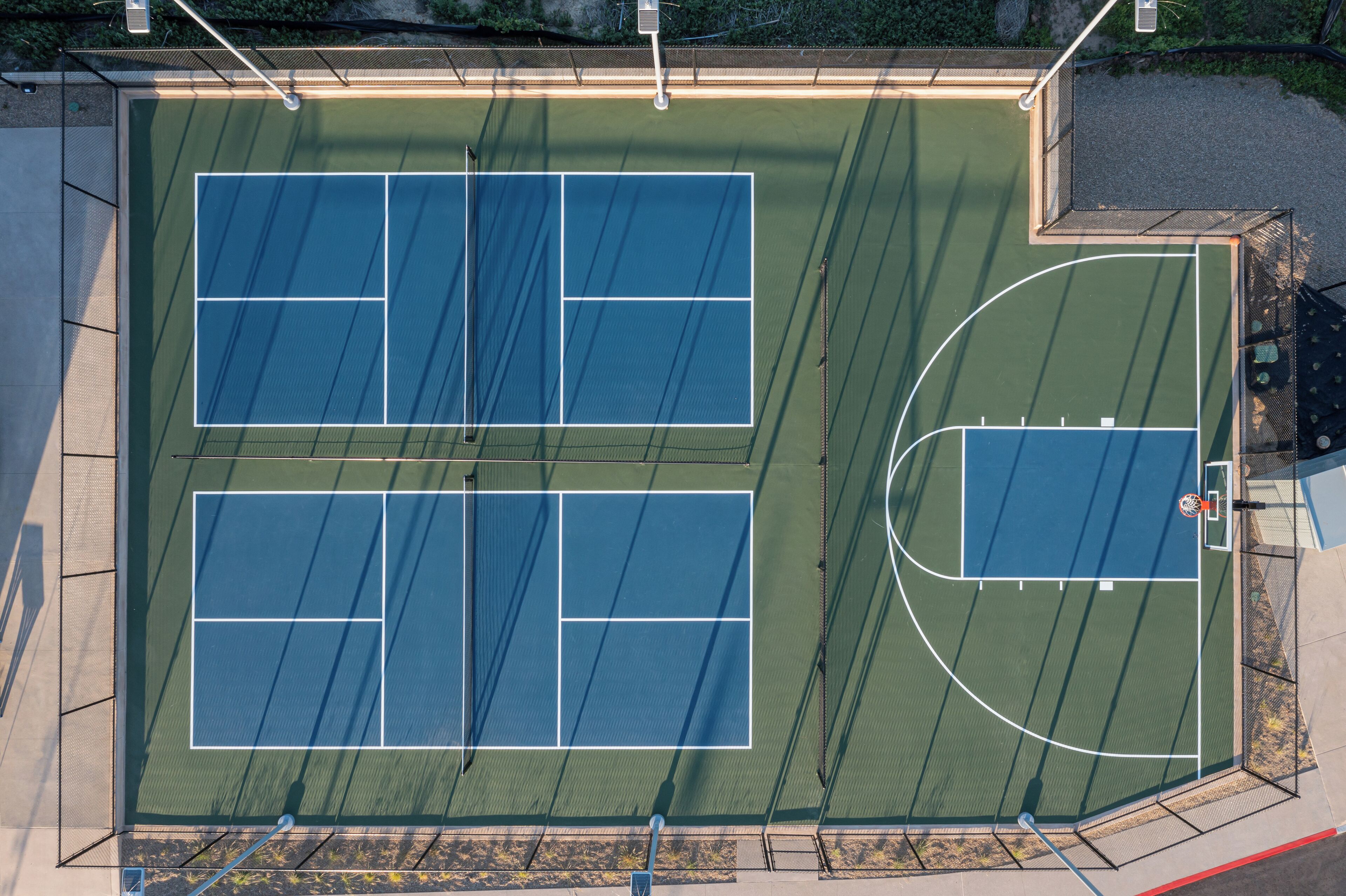 Vista aérea de una cancha de tenis con una cancha de baloncesto contigua.