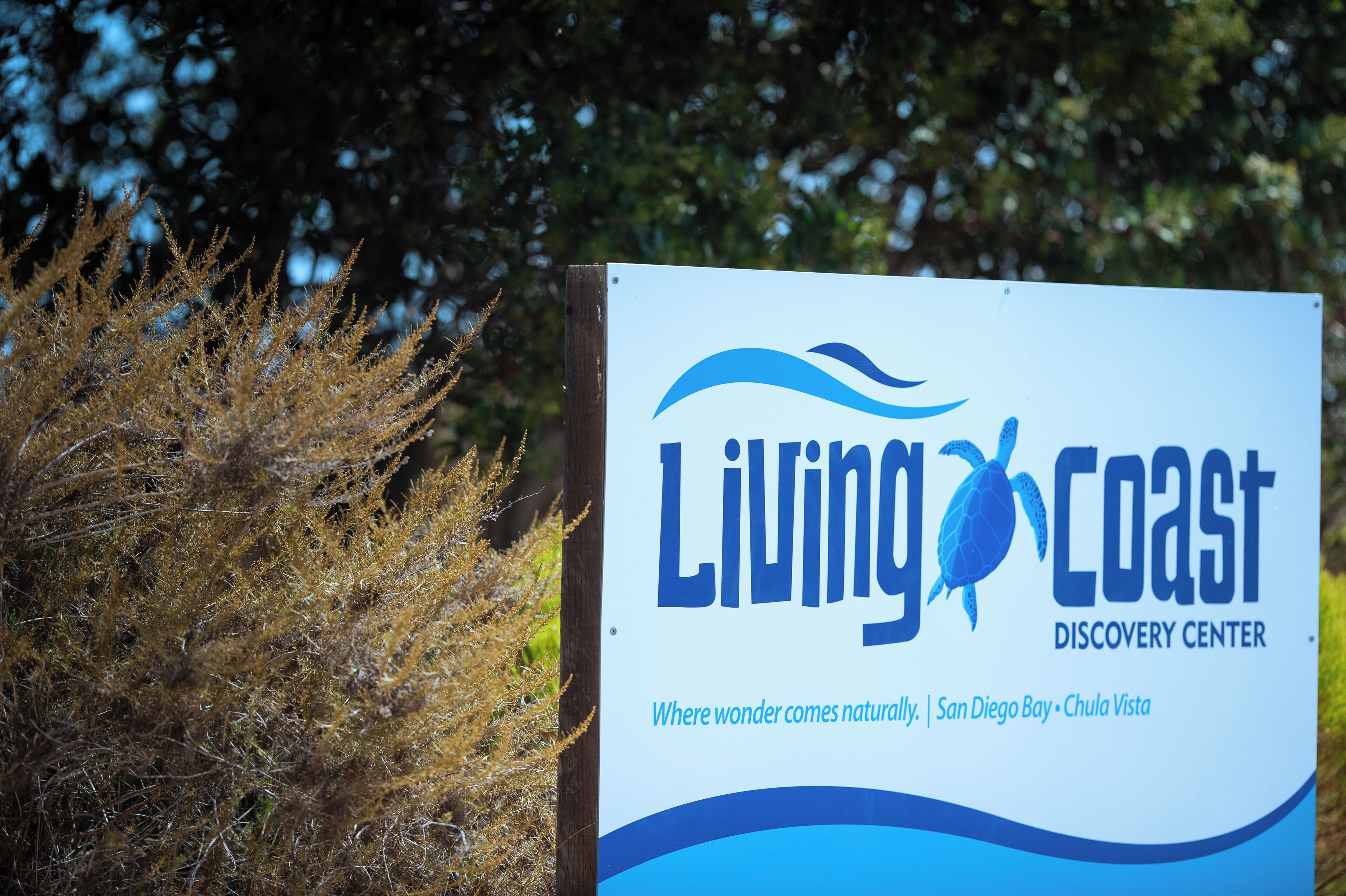 A sign for the Living Coast Discovery Center with a logo and text indicating its location in San Diego Bay, Chula Vista.