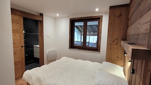 A bedroom with a bed, a window, and a wooden wall. - Titre Provisoire (Montgenèvre)