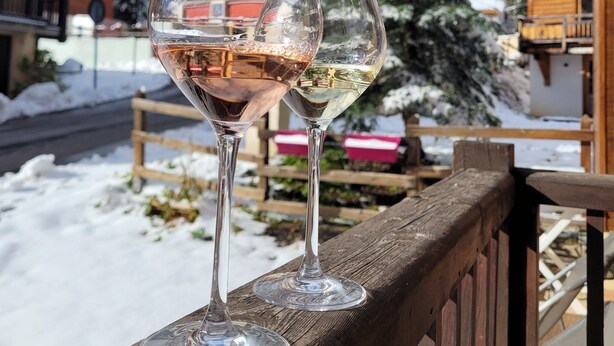 Two wine glasses on a wooden railing with a snowy landscape and buildings in the background. - Titre Provisoire (Montgenèvre)