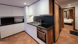 A compact kitchen with white cabinets, a black countertop, a built-in oven, and a sink. - Titre Provisoire (Montgenèvre)