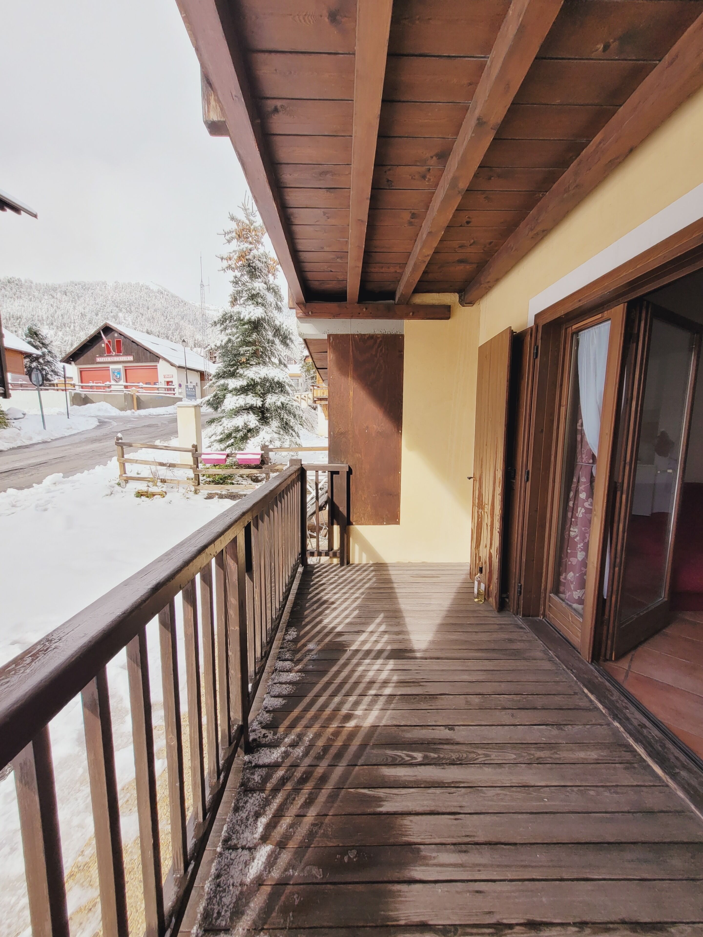 Ein hölzerner Balkon mit Blick auf eine verschneite Landschaft und ein Gebäude mit roter Tür.