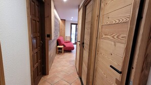 A hallway with wooden doors, a red chair, and a small table. - Titre Provisoire (Montgenèvre)
