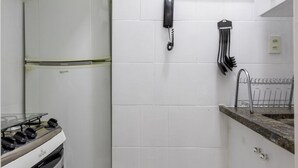 Una cocina compacta con azulejos blancos, estufa a gas, refrigerador y una ventana pequeña.