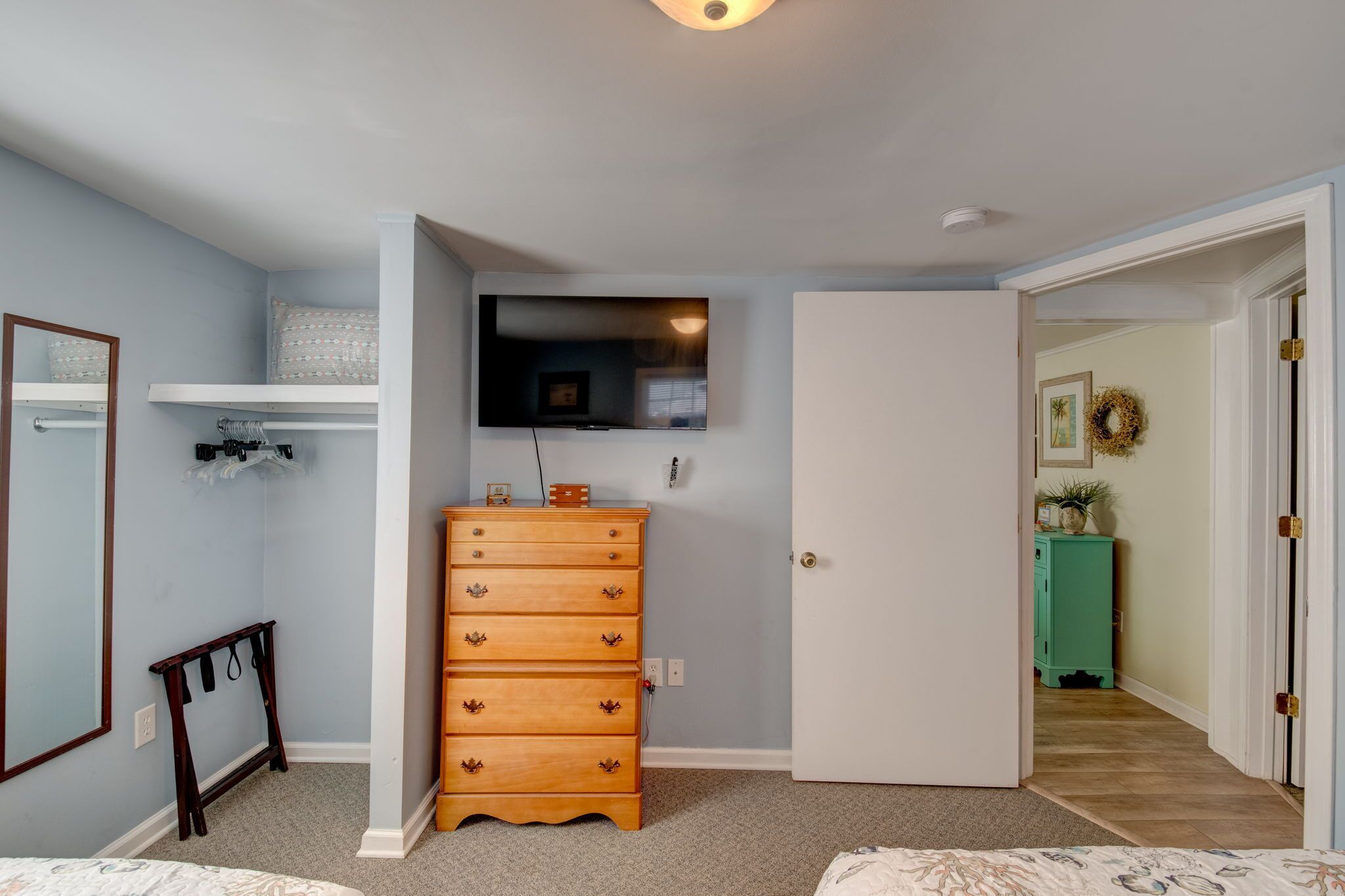 Un dormitorio con un aparador de madera, un televisor en la pared, un espejo y una puerta que da a otra habitación.