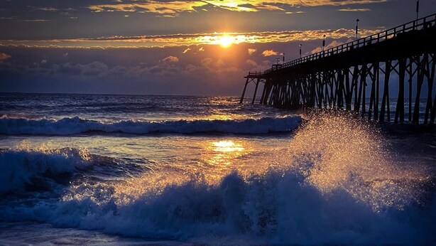 A pier extending into the ocean with waves crashing onto the shore. - Bungalow on 5th (Kure Beach)
