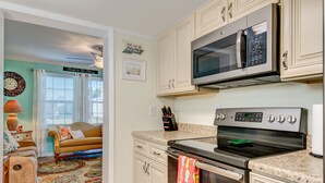 A kitchen with a microwave, oven, and a countertop with a knife block. - Bungalow on 5th (Kure Beach)