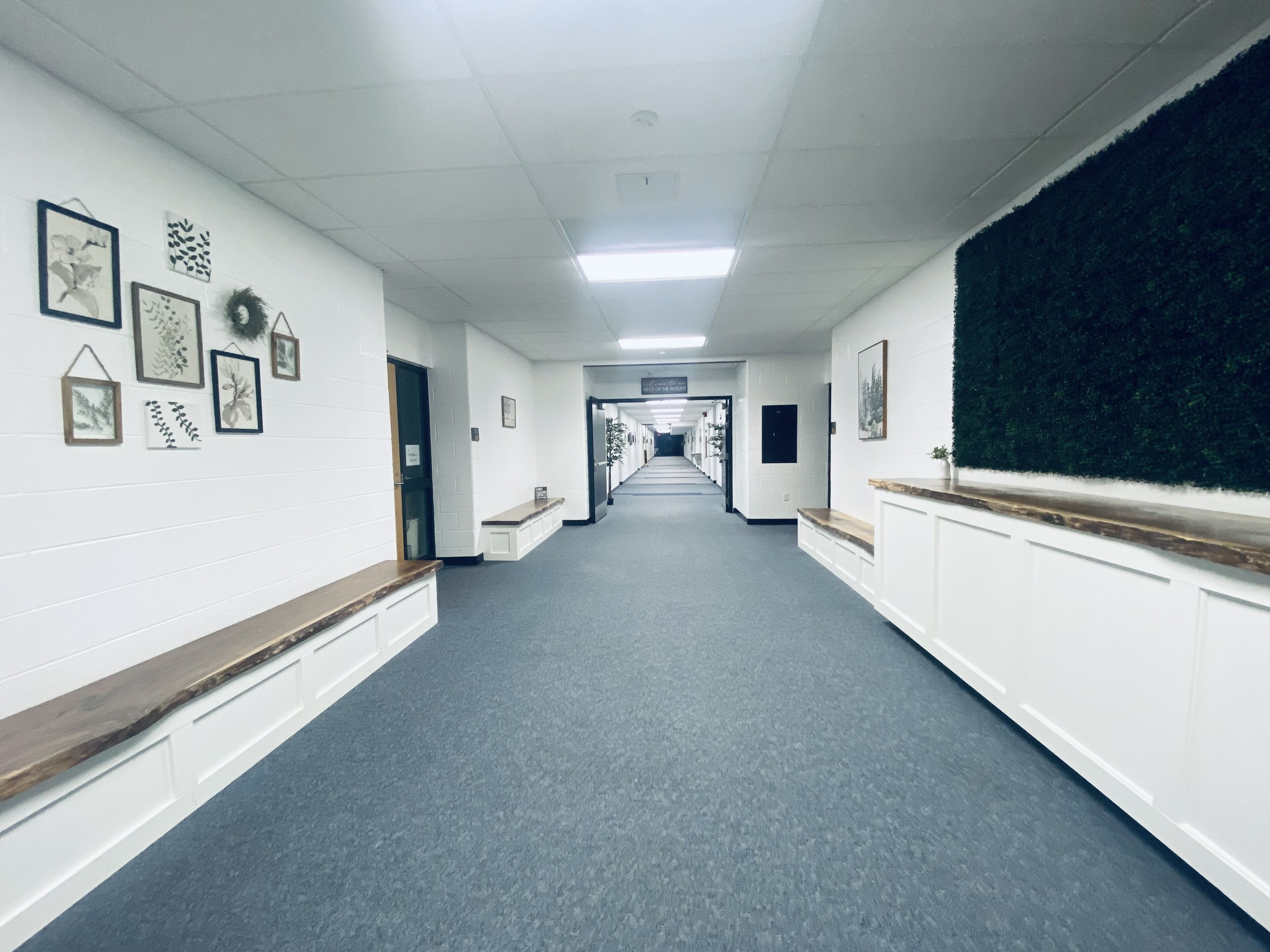A long, narrow hallway with white walls, a grey carpet, and a wooden bench on the left.