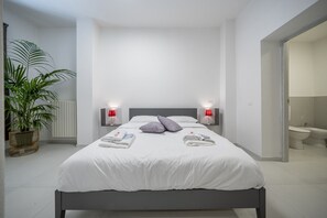 A modern hotel room with a large bed, bedside lamps, a potted plant, and a view of the bathroom. - [rua Muro] Piano Nobile Family (Modena)
