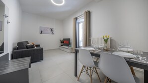 A modern living room with a grey sofa, a dining table set for four, and a flat-screen TV mounted on the wall. - [rua Muro] Piano Nobile Family (Modena)