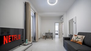 A modern living room with a flat-screen TV, a grey sofa, and a dining area with a table and chairs. - [rua Muro] Piano Nobile Family (Modena)