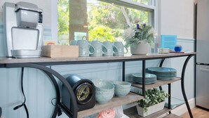Una cocina con ventana, una cafetera, una planta y varios platos en estantes.