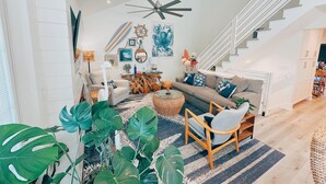 A spacious living room with a high ceiling, a modern ceiling fan, a staircase, and a dining area.