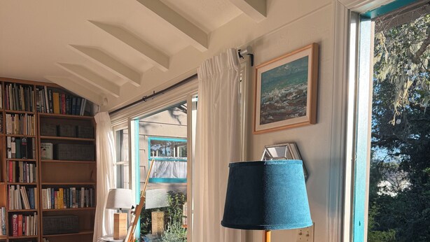 A room with a wooden desk, a chair, a lamp, a bookshelf, and a door with a view of greenery. - Quintessential Carmel Writer's Hideaway with Private Garden and Patio. (Carmel-by-the-Sea)
