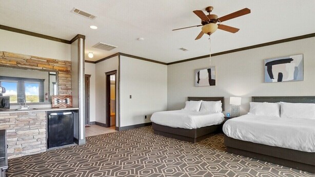 A hotel room with two beds, a kitchenette, a stone accent wall, and a patterned carpet. - MotorBoat Inn Suite 1 Pet Friendly (Graford)