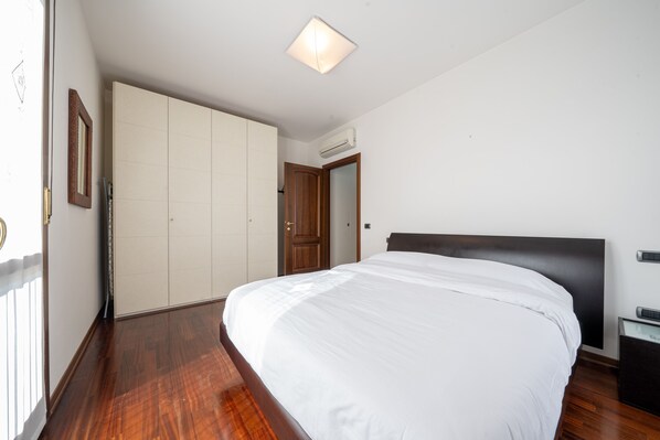 Ein Schlafzimmer mit einem großen Bett, Holzboden, einem Kleiderschrank und einer Deckenleuchte.