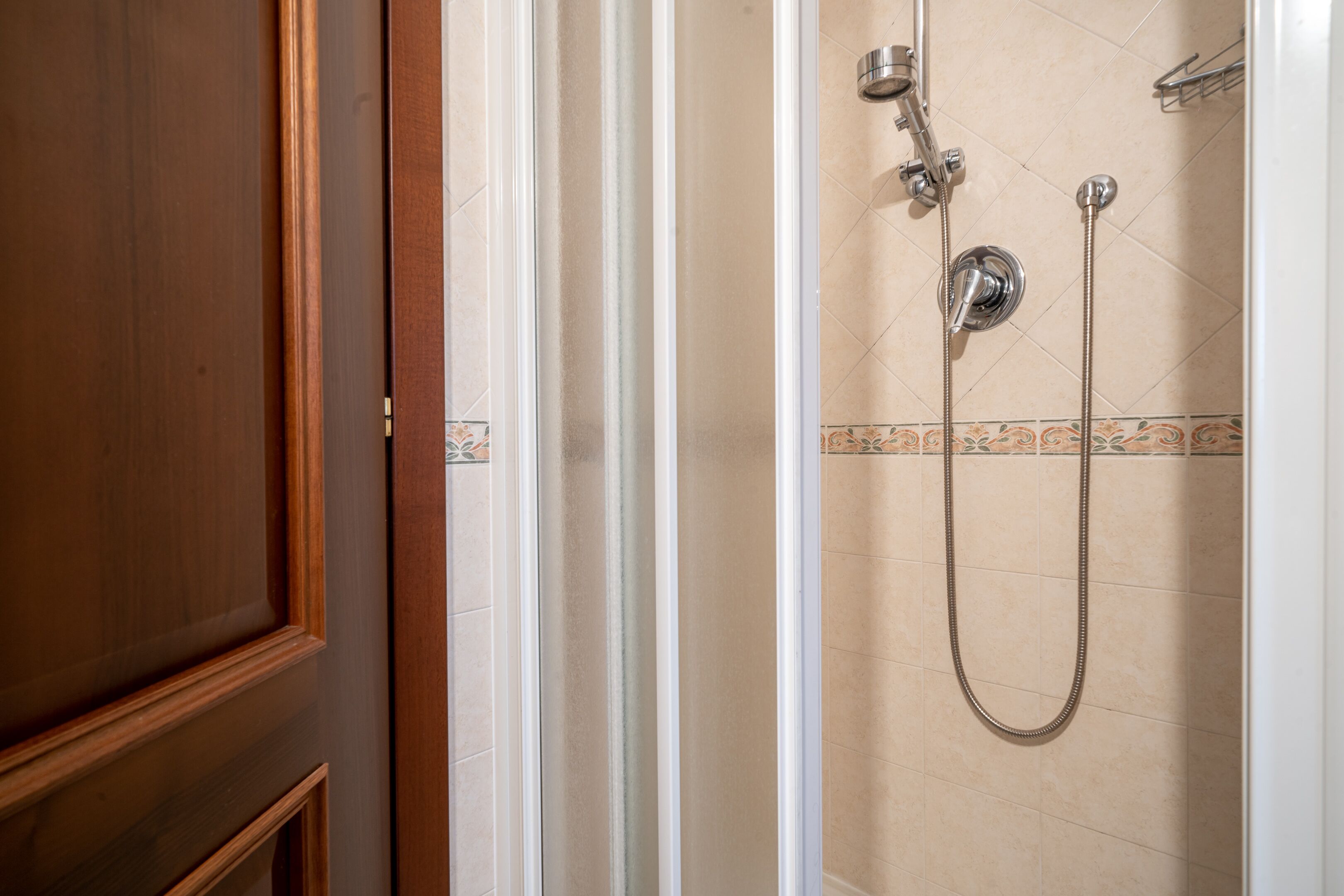 A shower area with a tiled wall, a showerhead, and a handheld shower attachment.